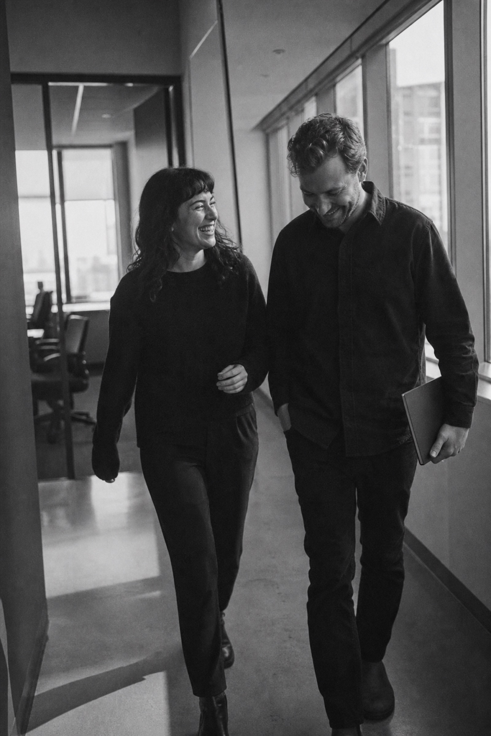 Two colleagues walking away from a conference room, one mid-laugh, the loose posture of relief